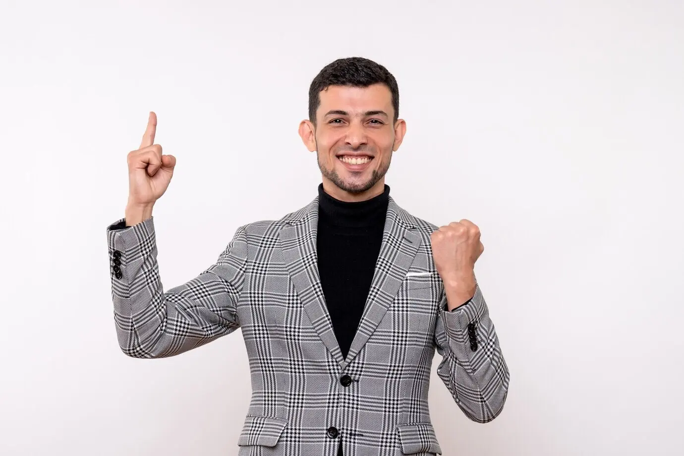 Front-facing view of a handsome male in a suit pointing at the ceiling while standing against a white background.